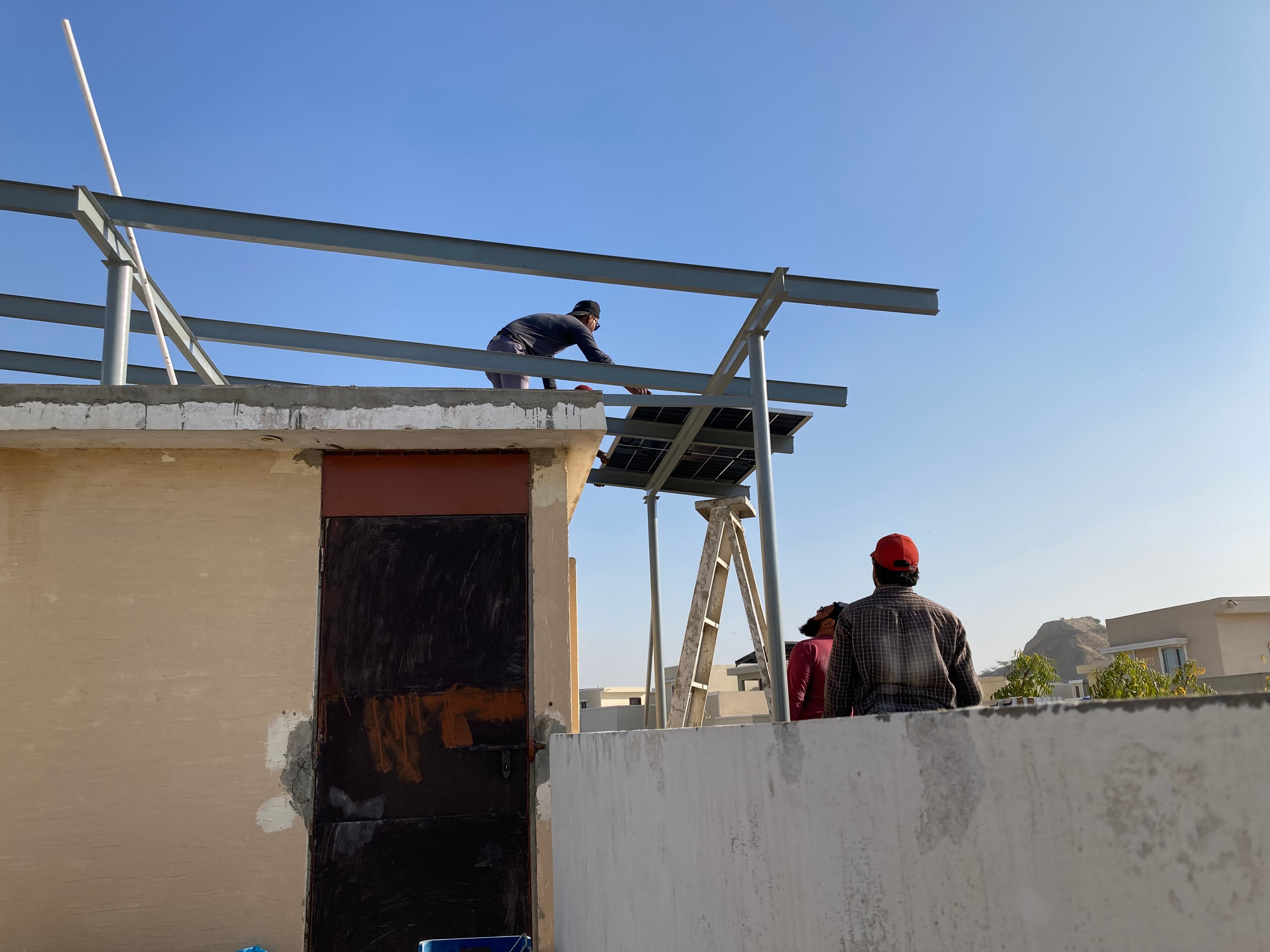 Worker setting a solar panel onto a new rooftop steel frame in Karachi.