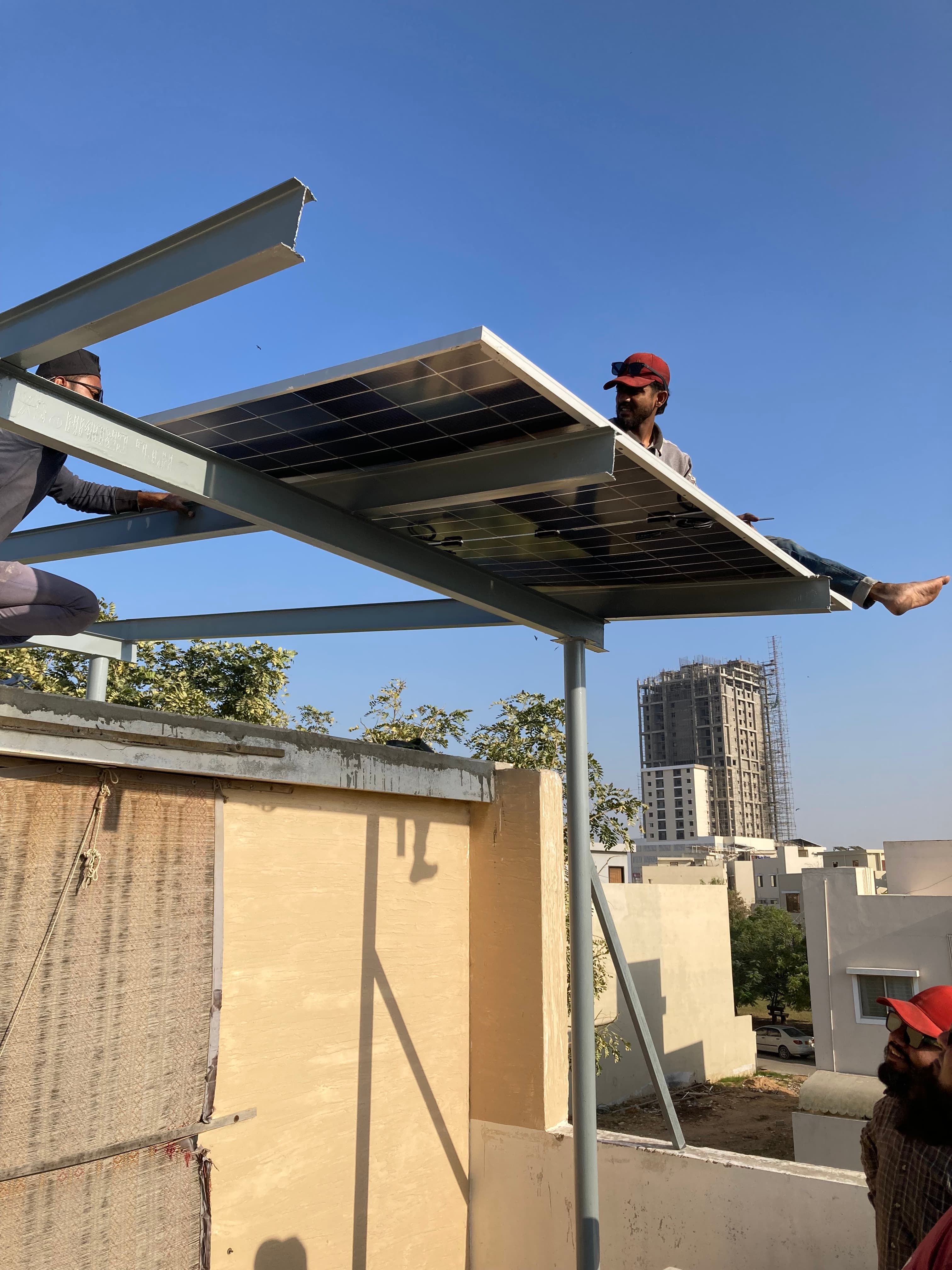 Technicians lifting and aligning a solar panel on a Karachi rooftop frame.