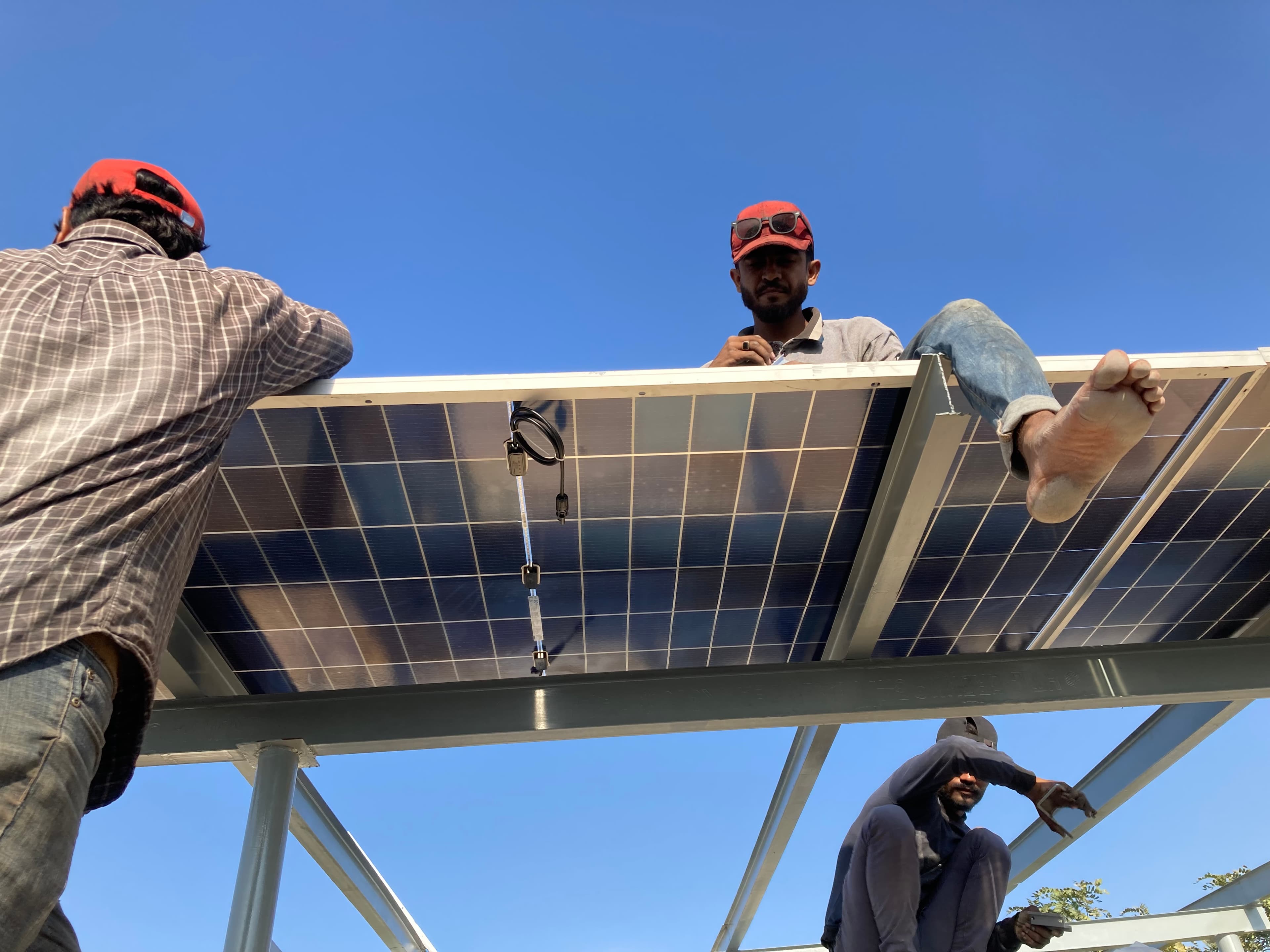 Low-angle view of technicians fixing a solar panel to a steel rooftop frame.