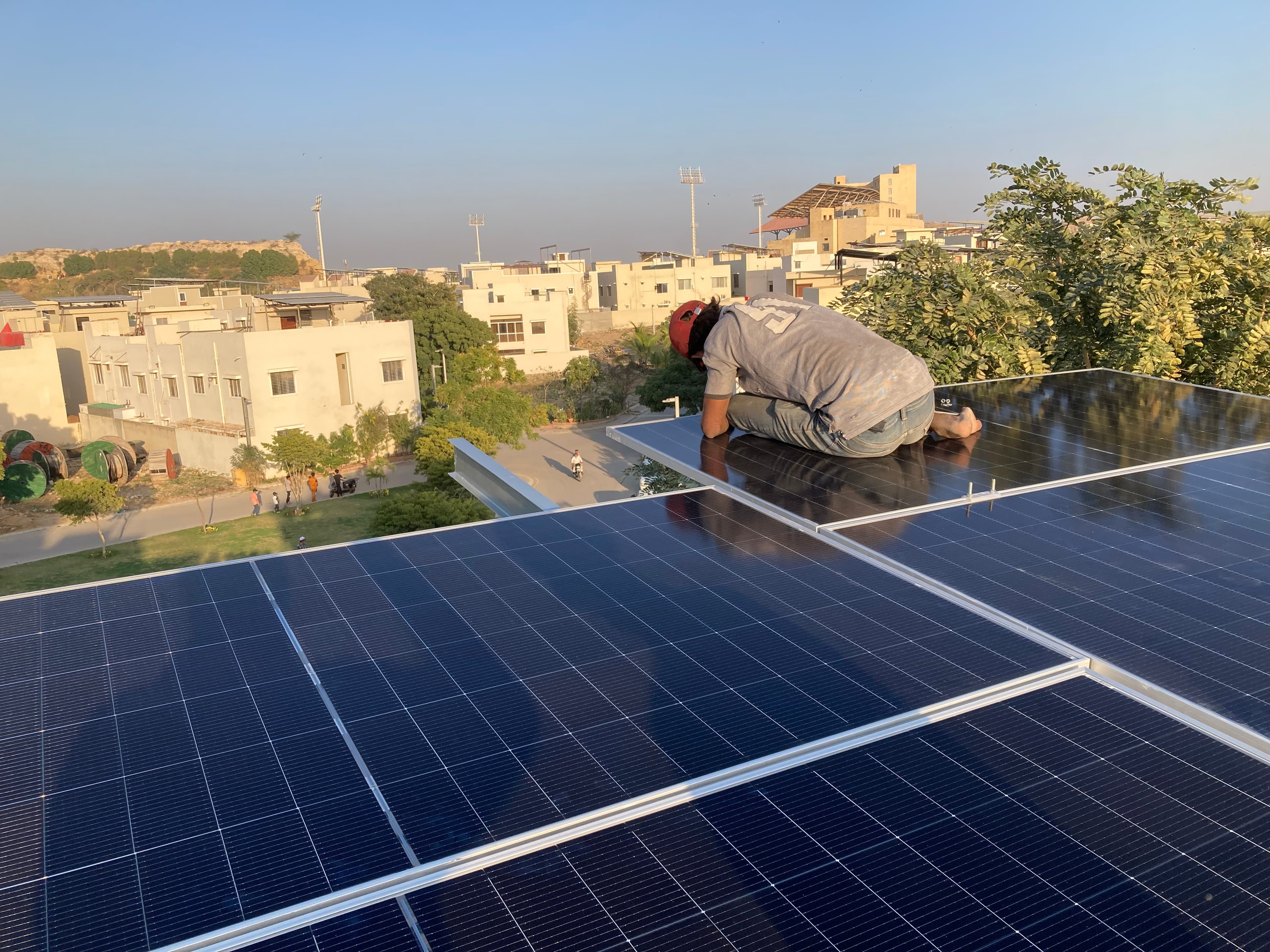 Installer fixing a rooftop solar panel into place above a Karachi residential block.