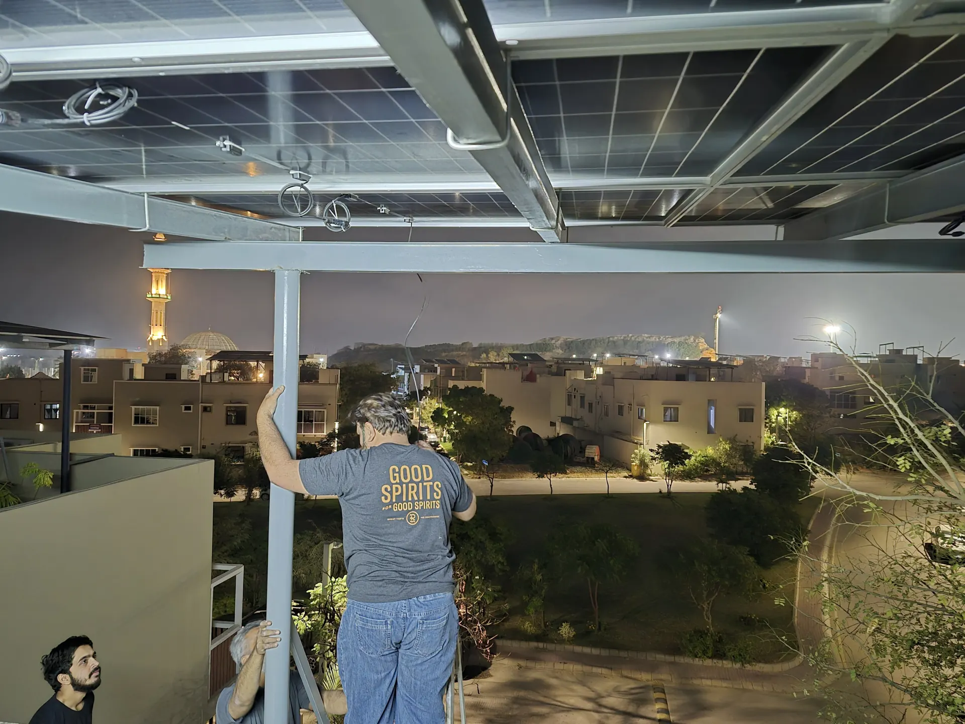 Karachi field crew working under a residential rooftop solar structure during evening installation.